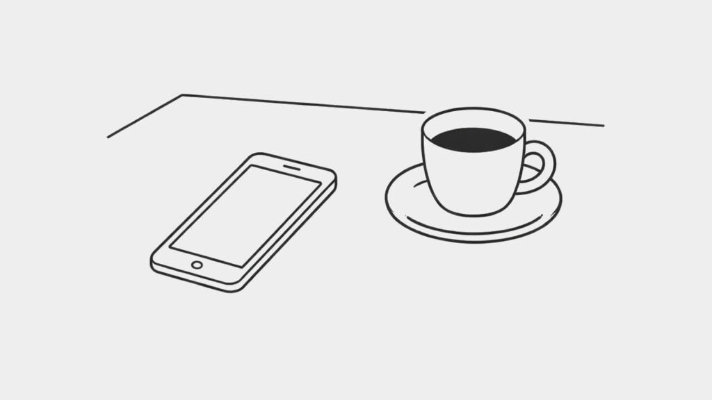 机の上に置かれたスマートフォンとコーヒー